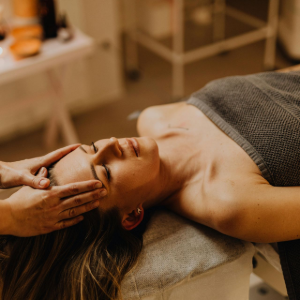 Woman receiving a facial massage on a spa table, covered with a towel.