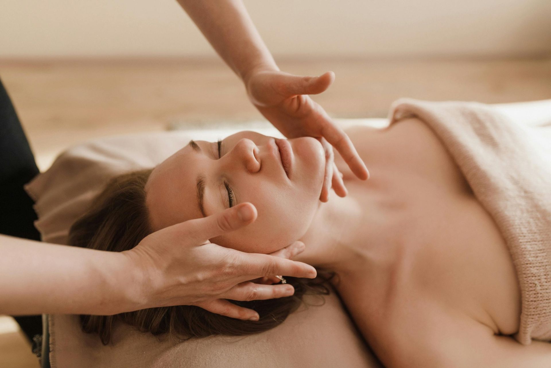 Massage therapist gently massaging a woman’s face and neck on a treatment table
