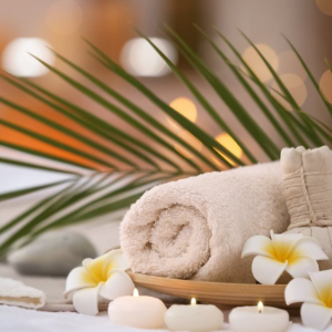 Spa towels with white flowers, candles, and palm leaves on a tray in a soft, warm setting