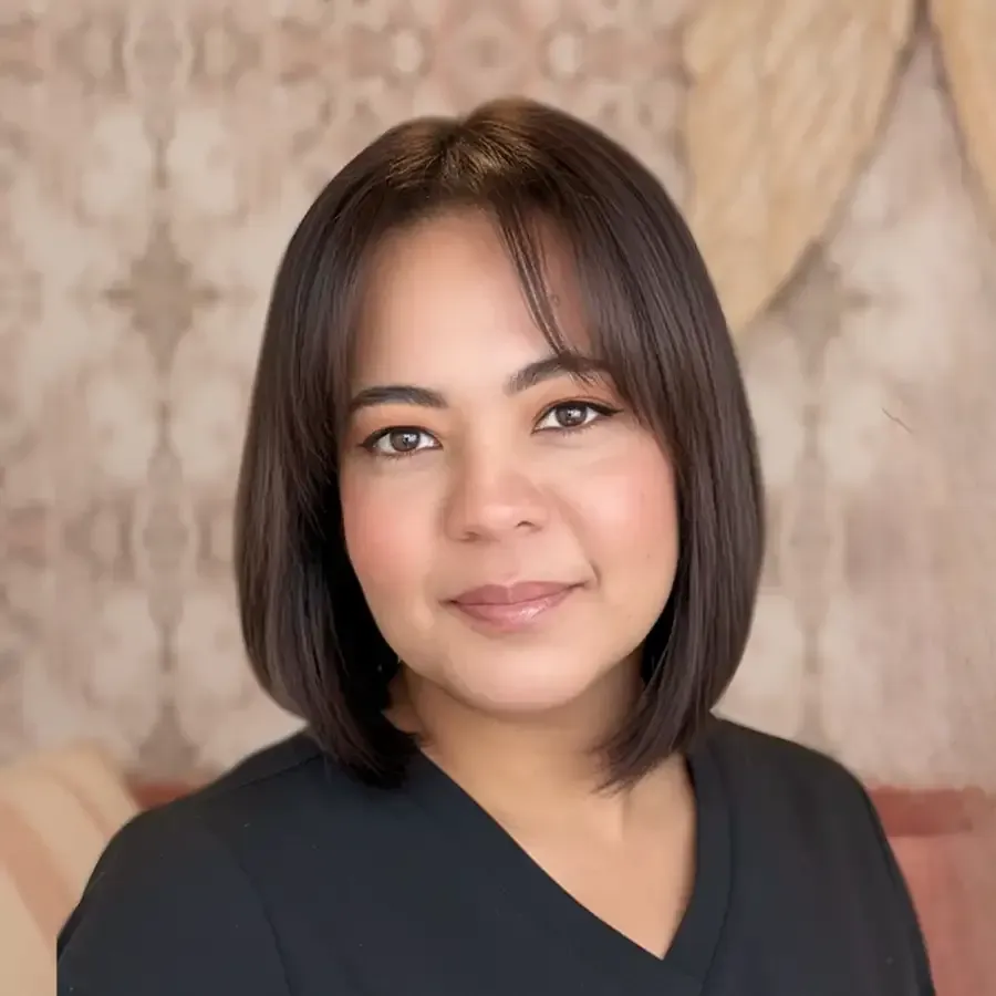Portrait of a person with a dark bob haircut, wearing a black top, against a soft patterned background