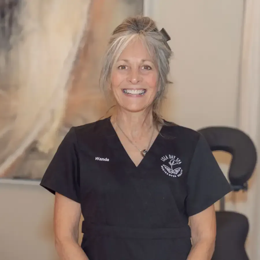 Smiling woman in black scrubs standing indoors, with a blurred abstract painting in the background.