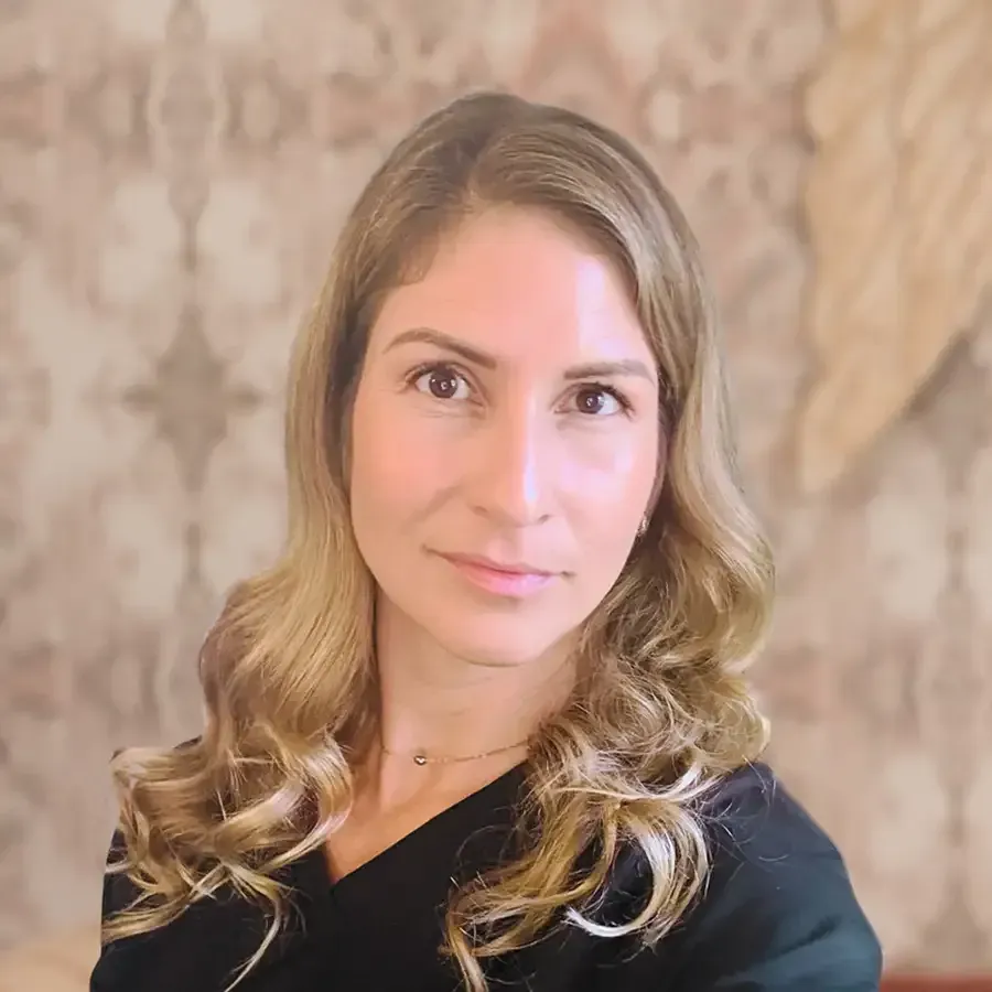 Portrait of a woman with wavy blonde hair, wearing a black top, against a beige textured background
