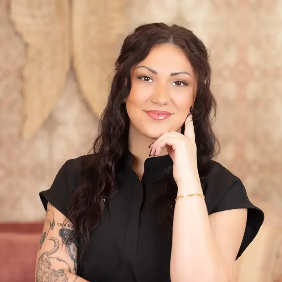 Portrait of a smiling woman in a black top, resting her chin on her hand against a warm textured background