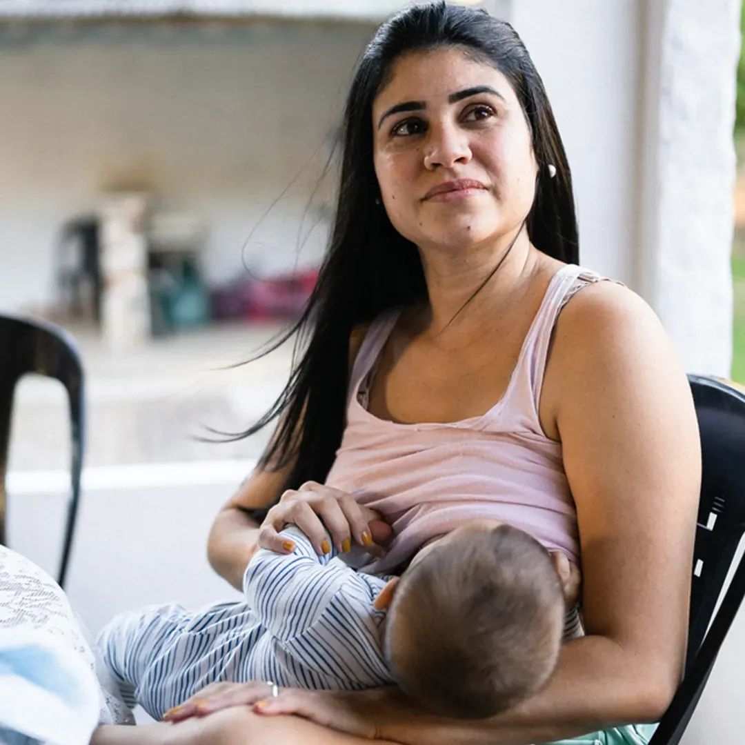 Uma mulher está sentada em uma cadeira amamentando um bebê.