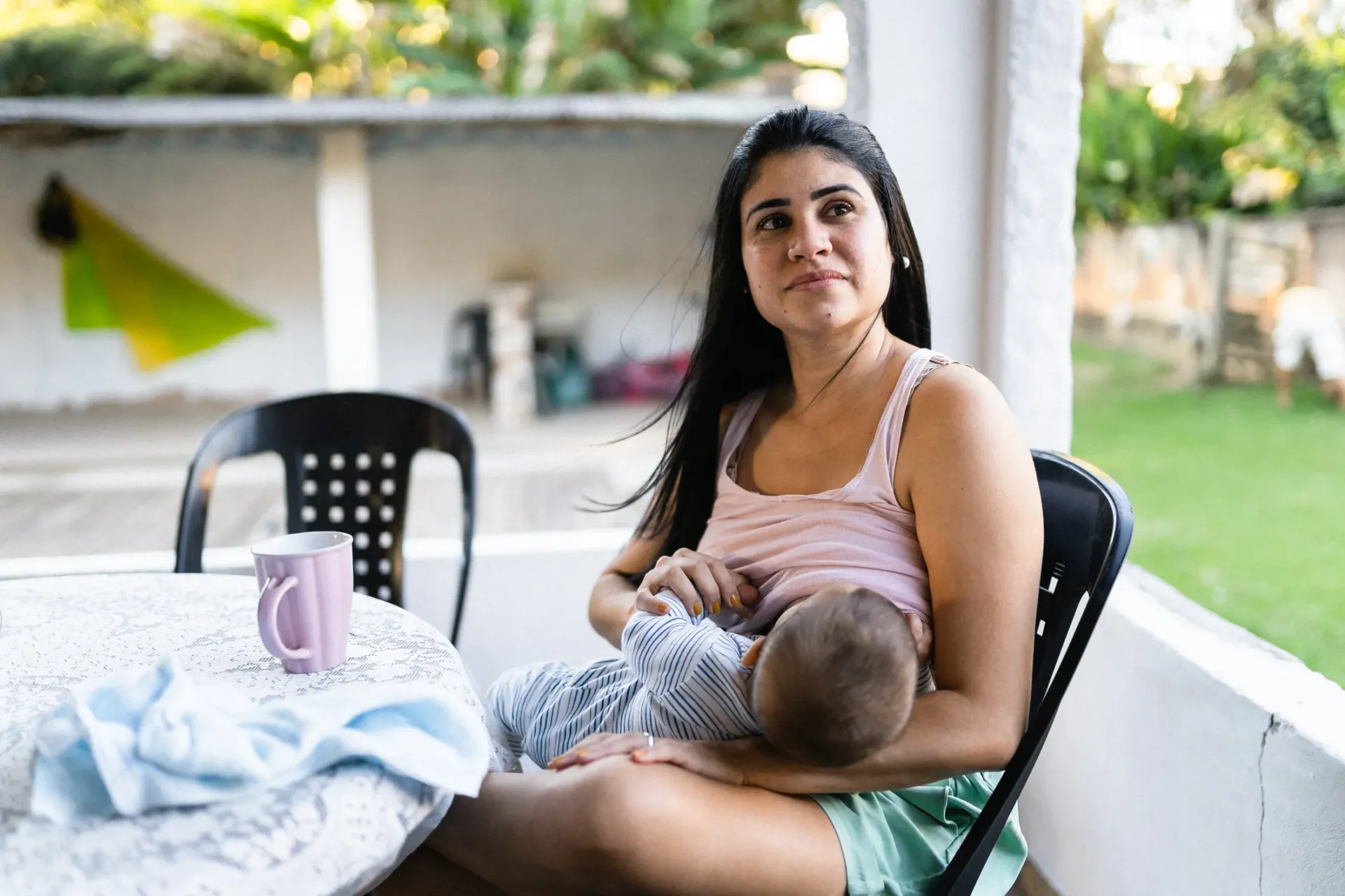 Uma mulher está sentada à mesa amamentando um bebê.