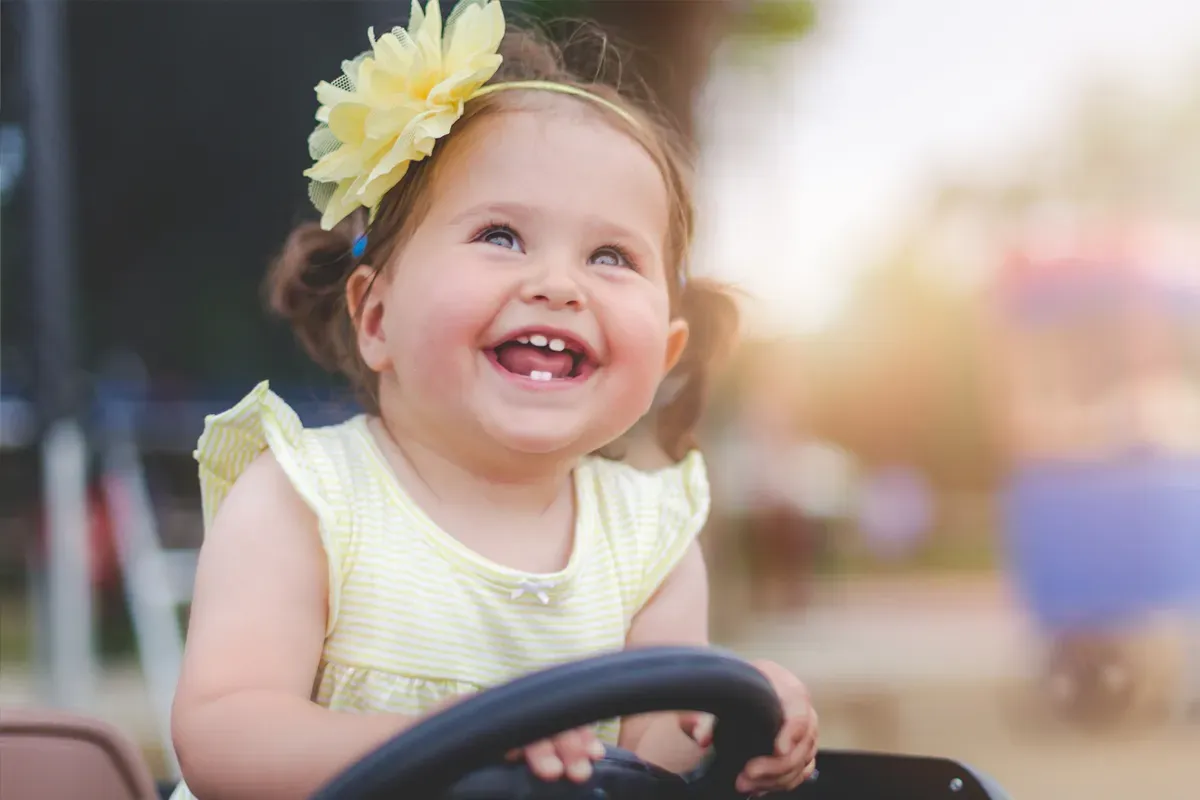 Uma menina está sentada em um carrinho de brinquedo e sorrindo.