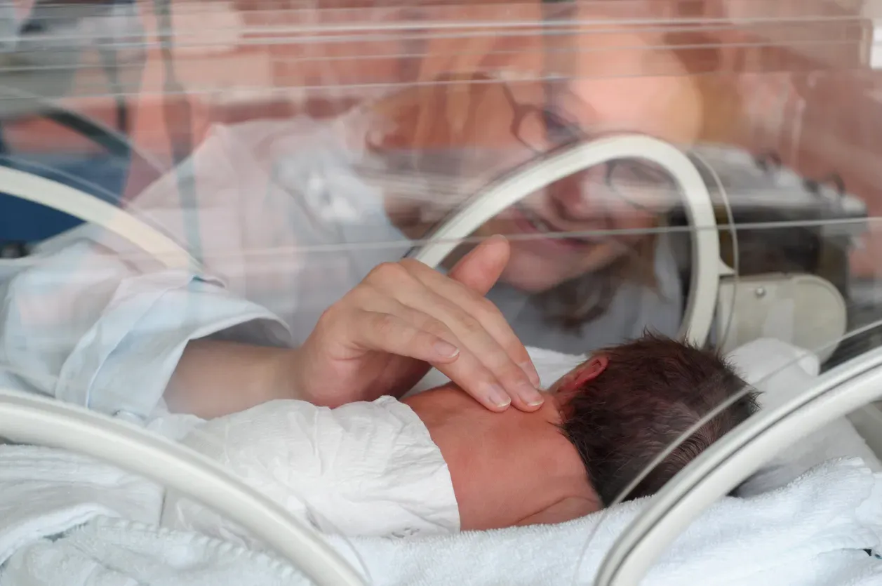 Uma mulher está acariciando um bebê recém-nascido em uma incubadora.