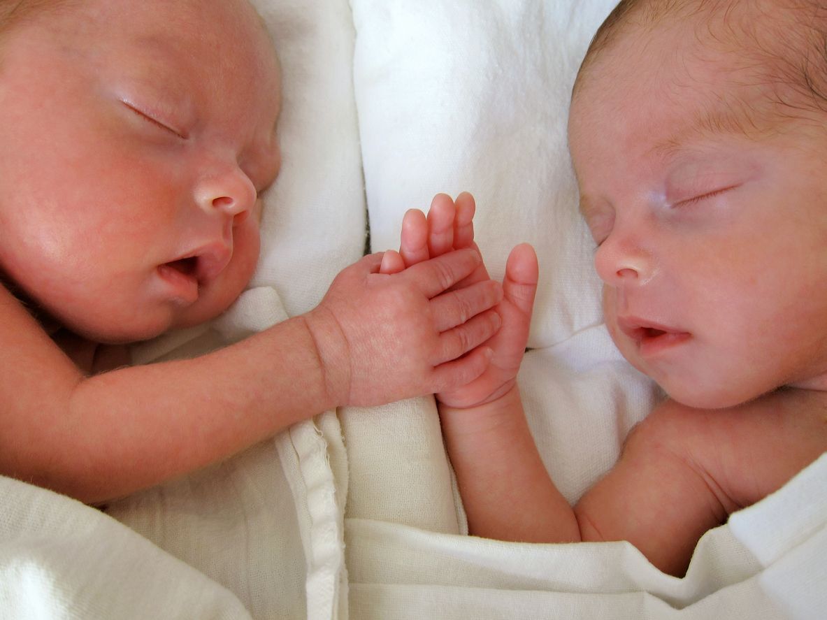 Dois recém-nascidos dormem um ao lado do outro e de mãos dadas