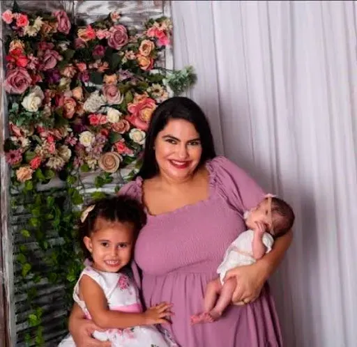 Uma mulher de vestido roxo está segurando um bebê e duas meninas.