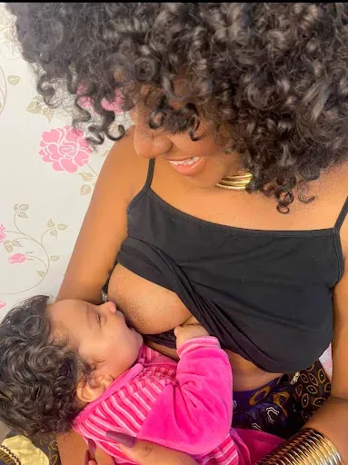 Uma mulher está amamentando um bebê com uma blusa rosa.