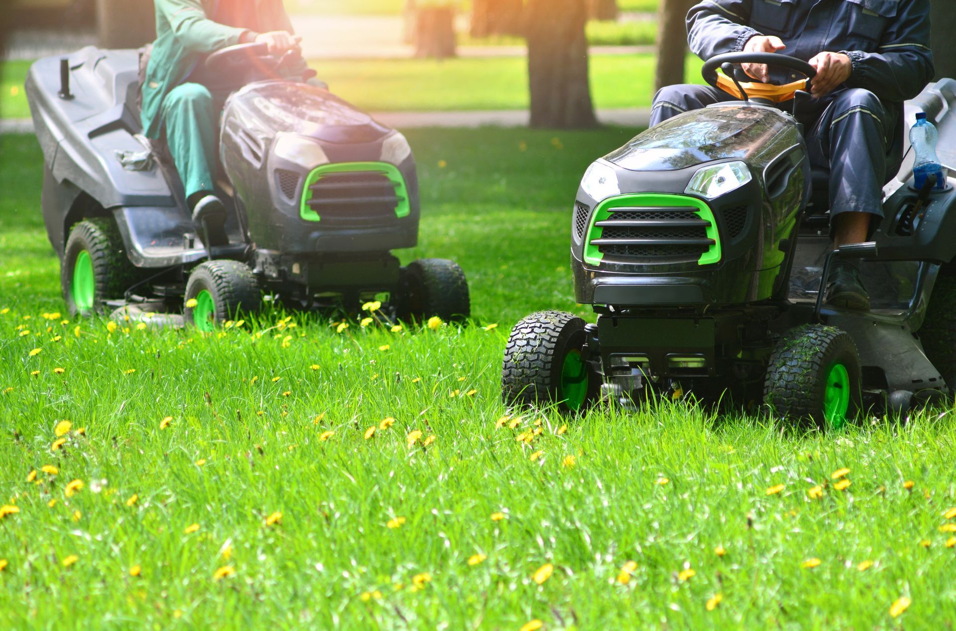 Two people mowing grass with riding lawnmowers in a sunny, grassy field. Two people mowing grass with riding lawnmowers in a sunny, grassy field.