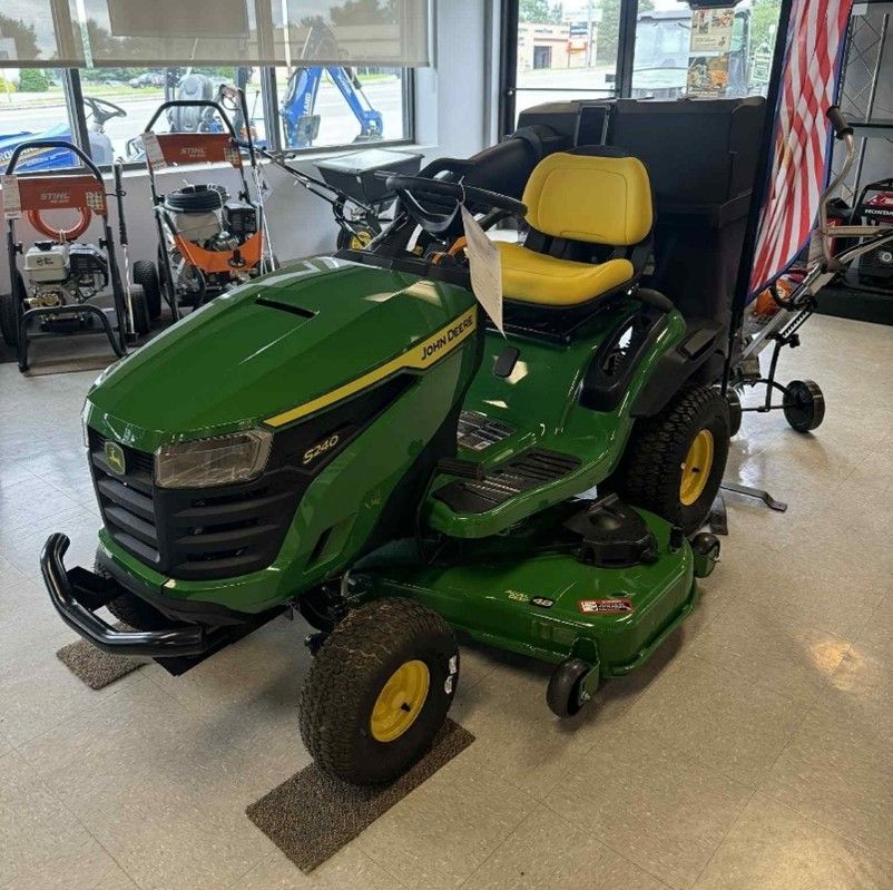 Green John Deere riding lawnmower with yellow seat and wheels in a store setting. Green John Deere riding lawnmower with yellow seat and wheels in a store setting.