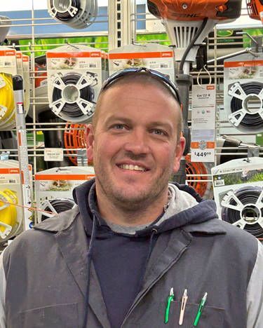 A man is smiling in front of a display of tools in a store.