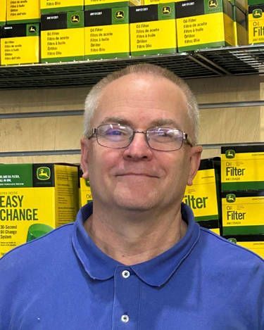 A man wearing glasses and a blue shirt is standing in front of boxes of john deere filters.