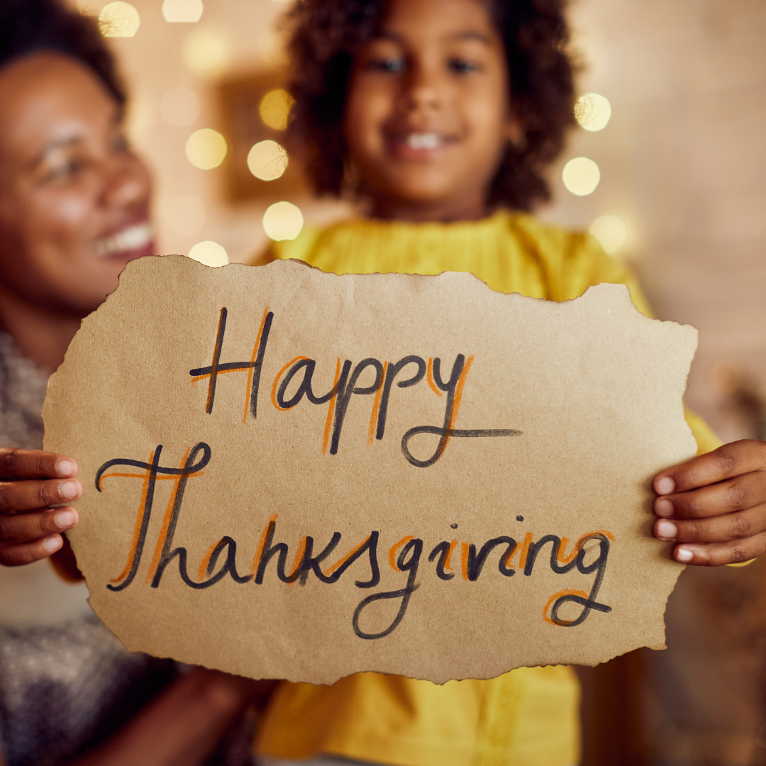 A woman and child are holding a piece of paper that says happy thanksgiving