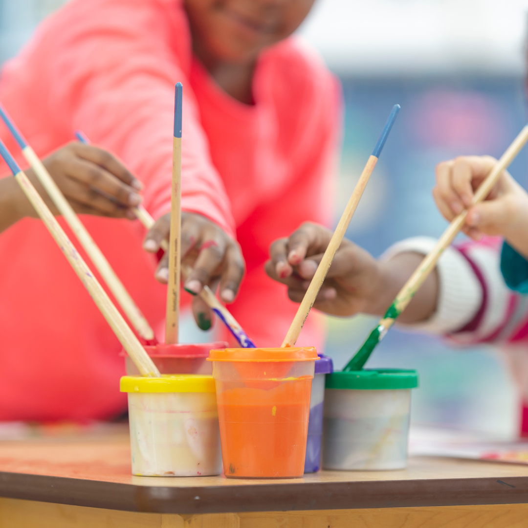 A group of children are painting with brushes and paints on a table.