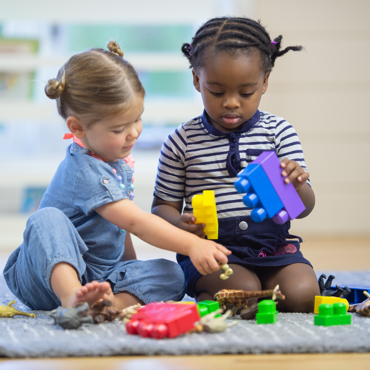 Two little girls are sitting on the floor playing with toys.