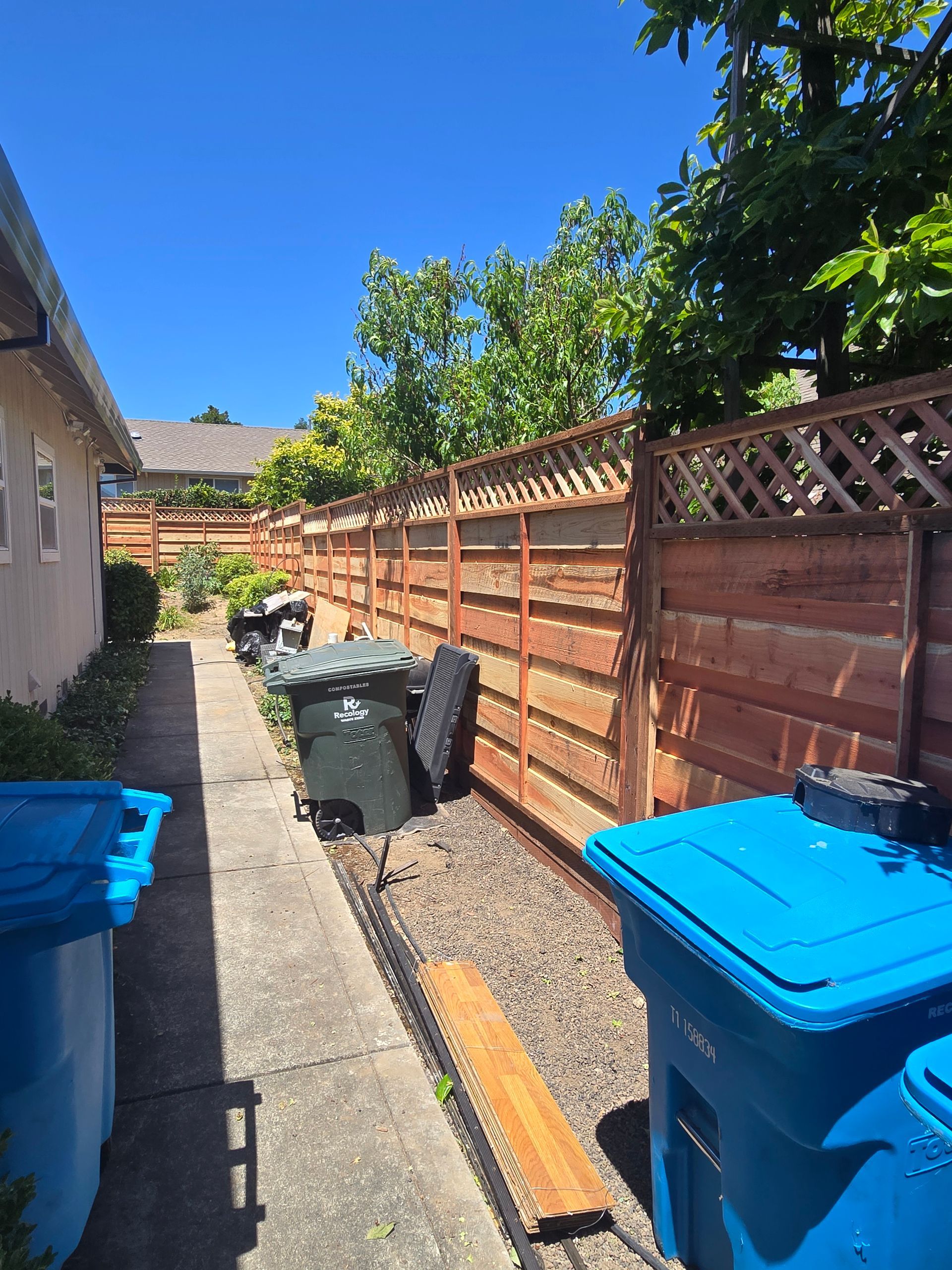 A wooden fence is surrounded by trash cans and trees