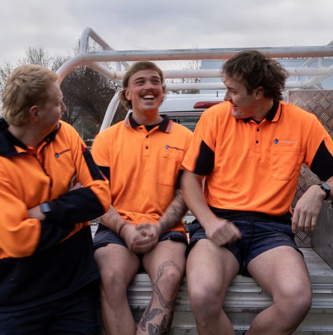 Three Men in Orange Shirts Are Sitting on the Back of a Truck — BJ Heating & Cooling in Beechworth, VIC
