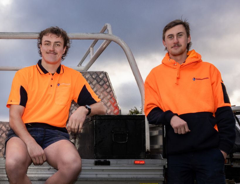 Two Men in Orange Shirts Are Sitting on the Back of a Truck — BJ Heating & Cooling in Holbrook, NSW