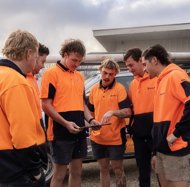A Group of Men in Orange Shirts Are Looking at a Tablet — BJ Heating & Cooling in Beechworth, VIC