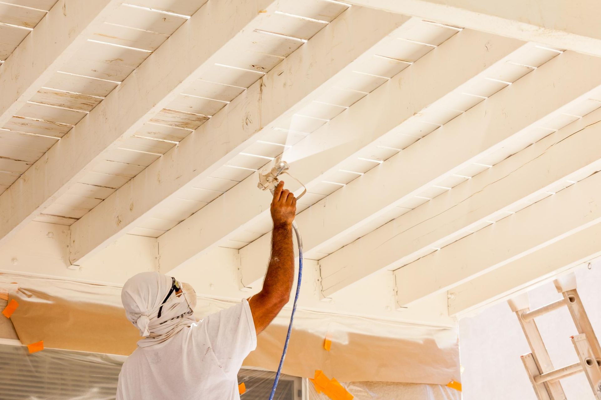 Man in protective gear sprays paint onto a white wooden ceiling.