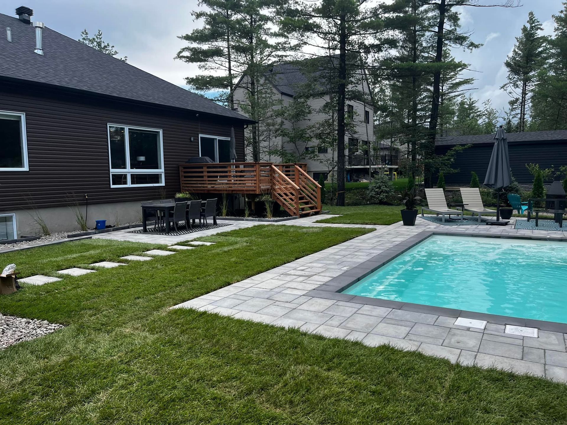 Jardin avec une maison brune, une terrasse, une piscine et une pelouse verte.
