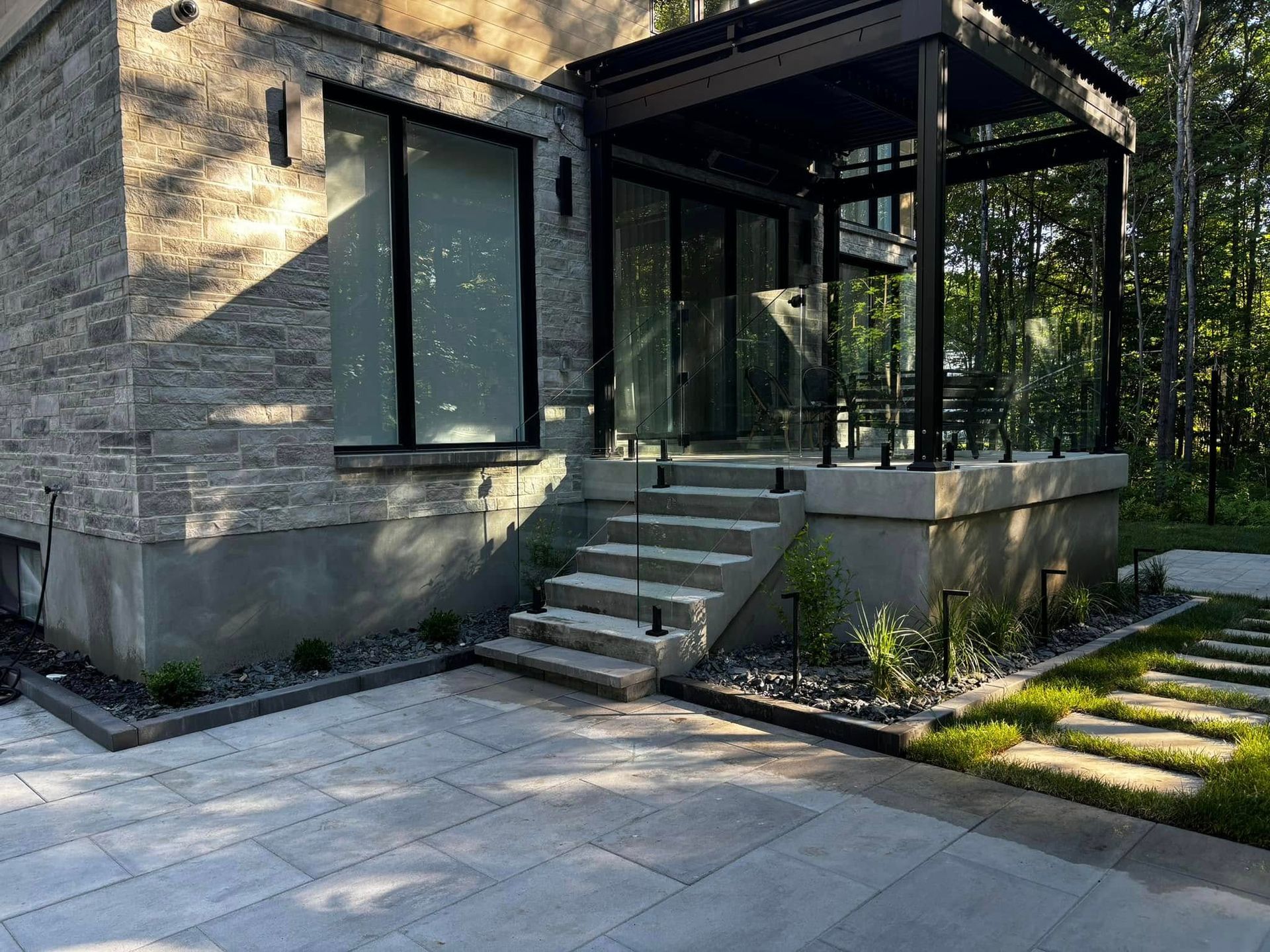 Extérieur de maison moderne avec façade en pierre, marches, balustrade en verre et terrasse.