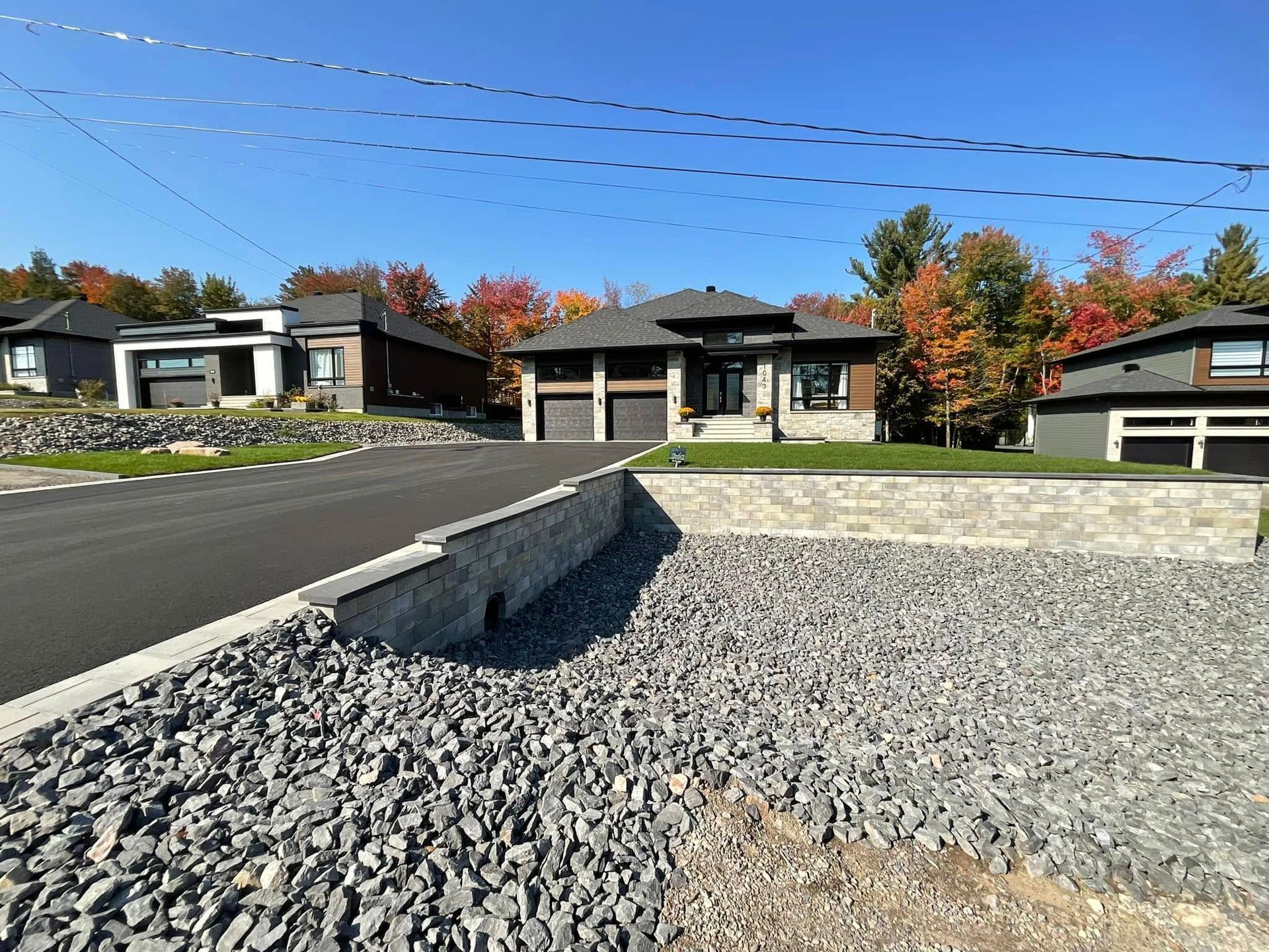 Maison moderne avec allée noire, lit de gravier gris et feuillage d'automne.