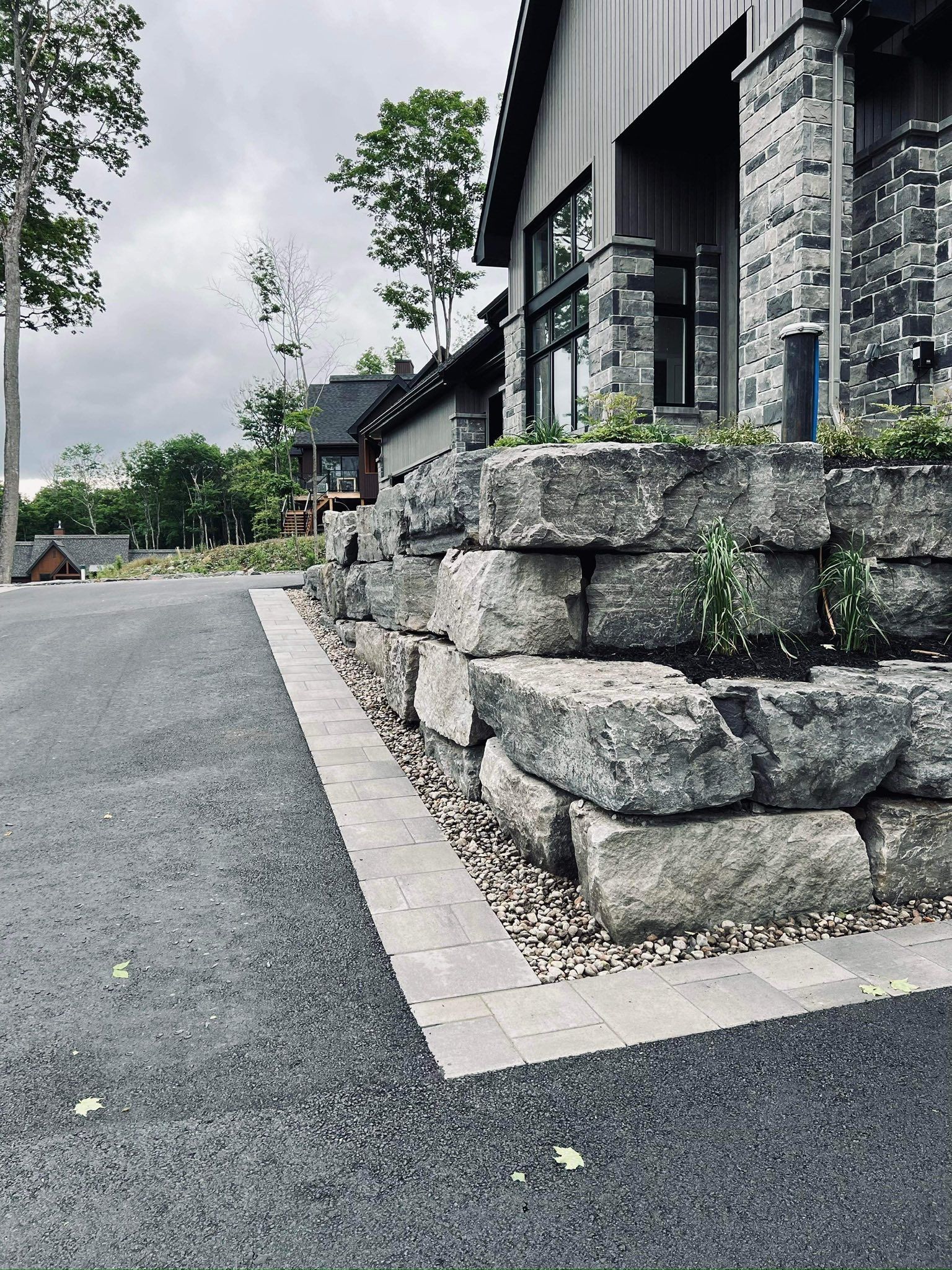 Exterior of a modern building with a stone retaining wall and a gravel driveway on an overcast day.