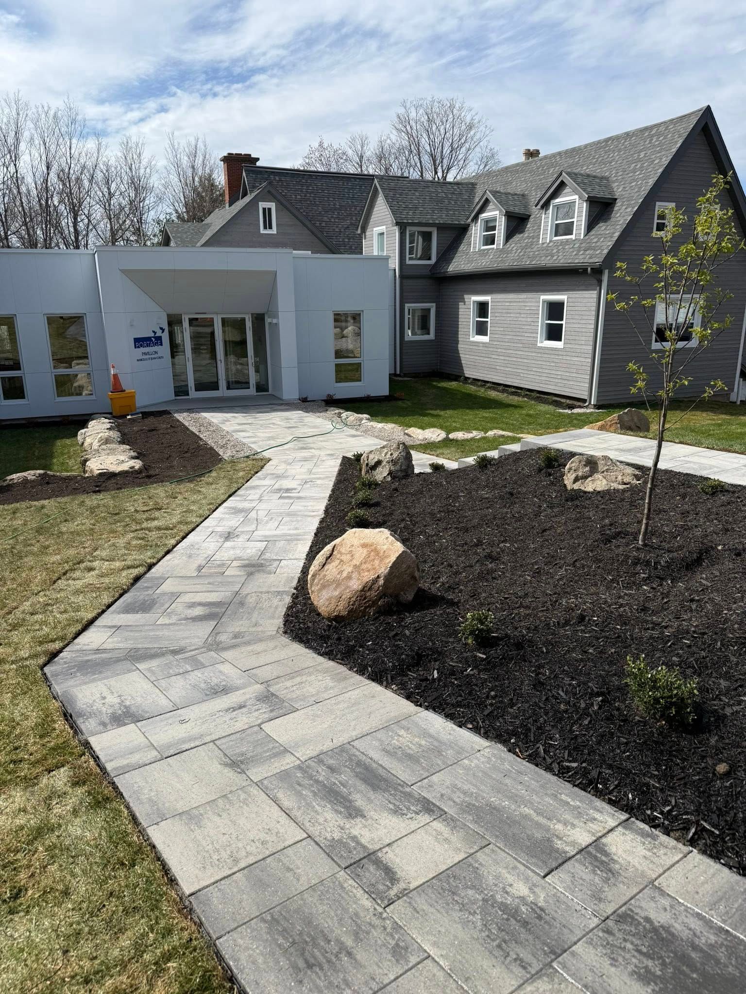 Extérieur d'un bâtiment avec une allée pavée. Le bâtiment possède une extension moderne et un toit gris traditionnel.