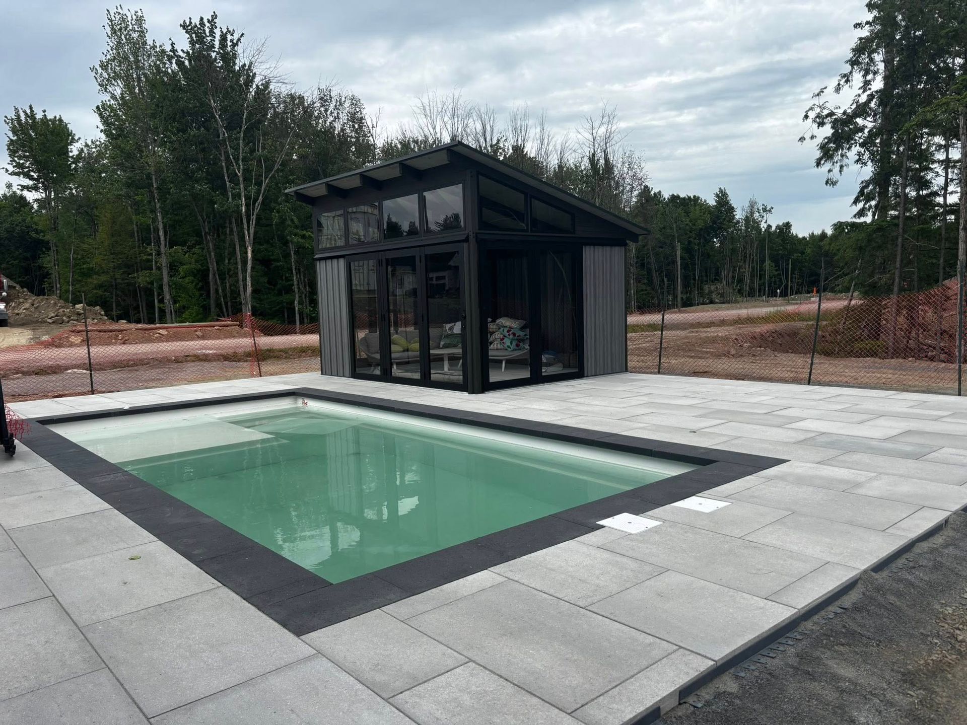 Piscine aux finitions gris foncé, entourée de dalles gris clair. Clôture à cadre noir en arrière-plan.