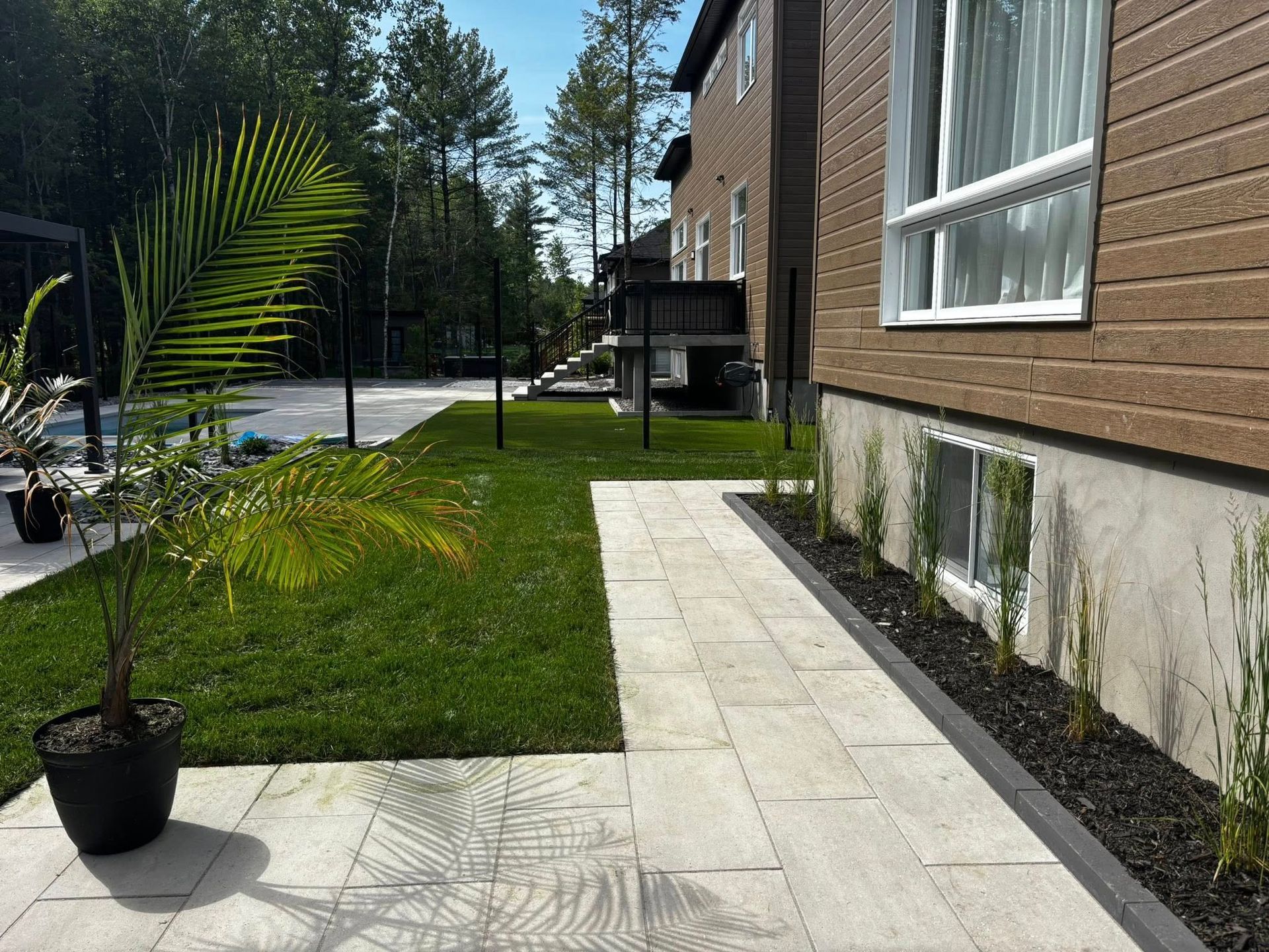 Chemin de pierres longeant une maison avec une pelouse et un palmier en pot.