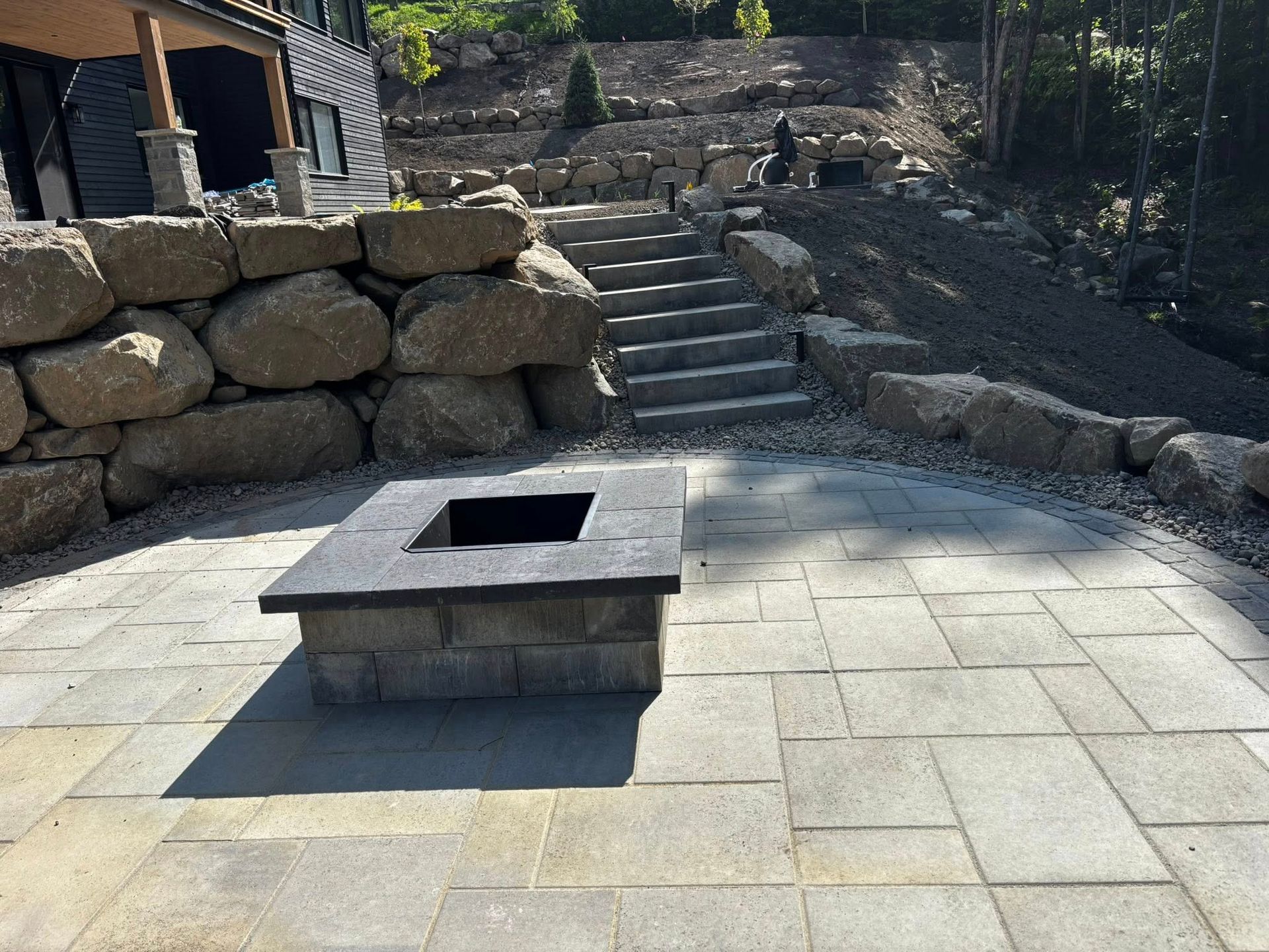 Terrasse en pierre avec foyer, escaliers et murs de soutènement en gros rochers.