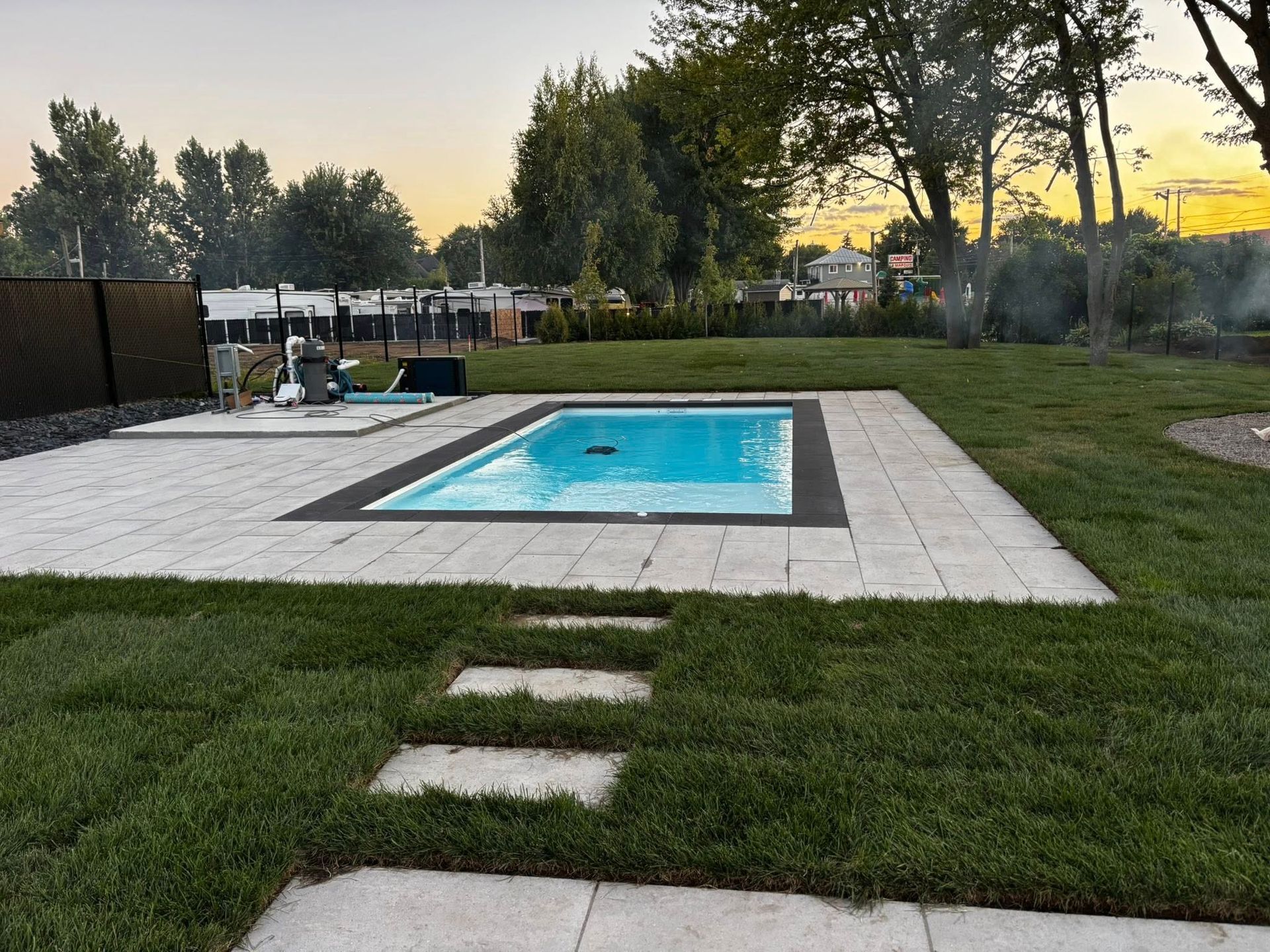 Piscine rectangulaire avec dallage clair, entourée de pelouse et de quelques pas japonais. Arbres en arrière-plan.