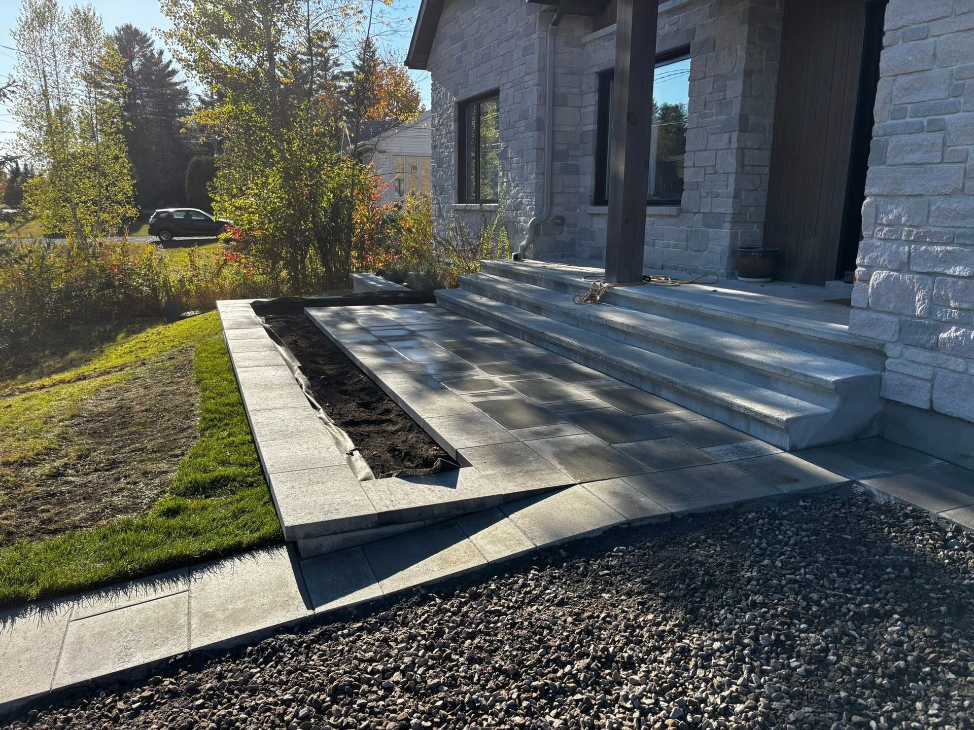 Vue extérieure d'une maison avec des marches en pierre et une jardinière à côté d'un chemin de gravier et d'une pelouse.