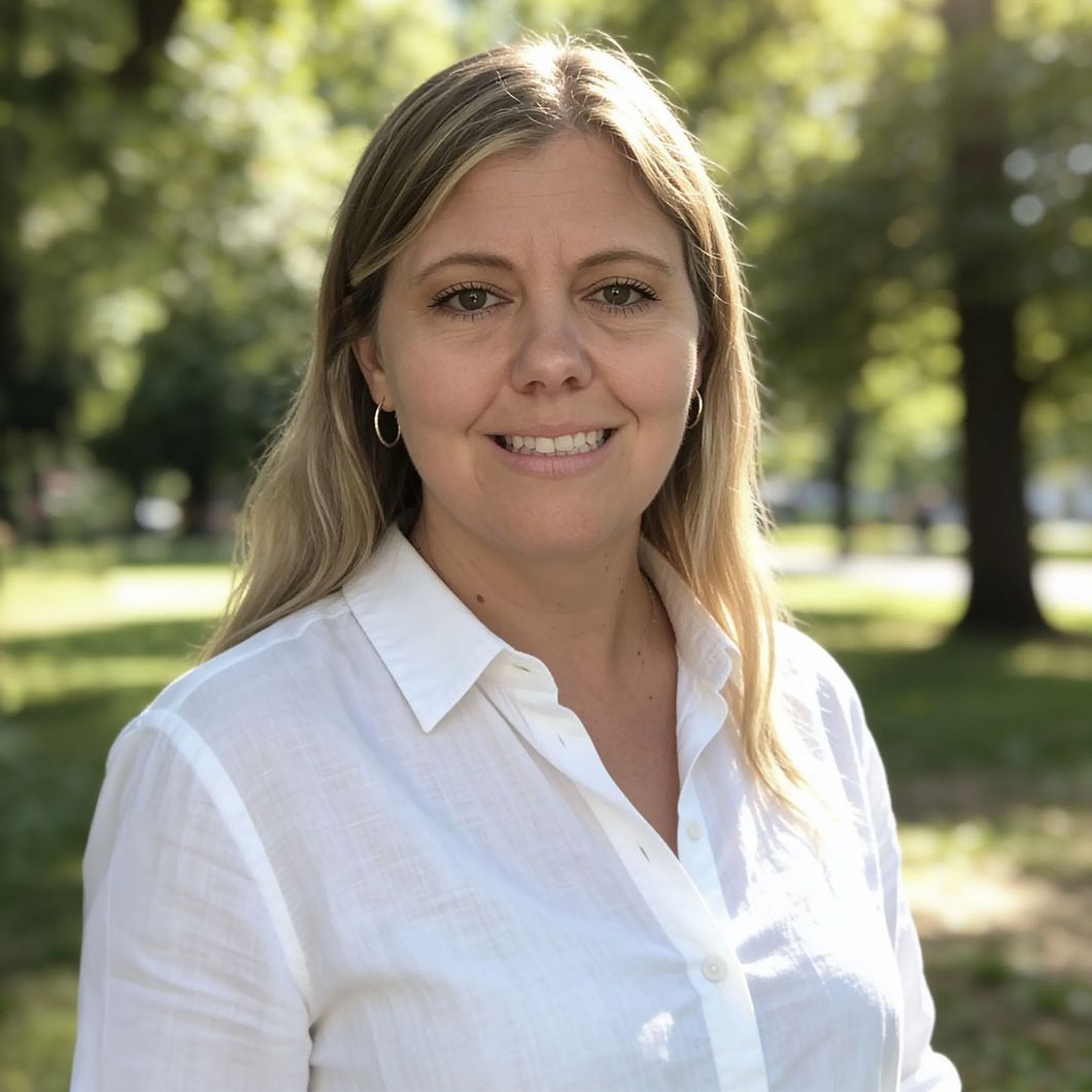 Smiling woman in a white blouse standing outdoors in a sunlit park