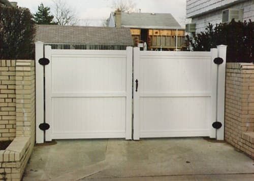 A white gate is open in front of a brick wall