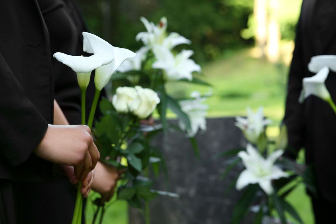 Mano sosteniendo lirios blancos en un jardín con un fondo verde difuminado.