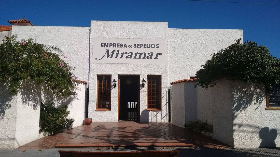Fachada blanca con letrero que dice “Empresas y Cielos Micamar”, enmarcada por árboles bajo un cielo azul.