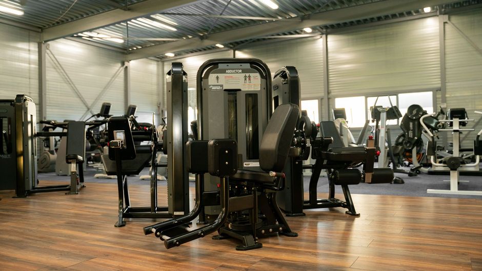 Een sportschool vol met fitnessapparatuur en een houten vloer.