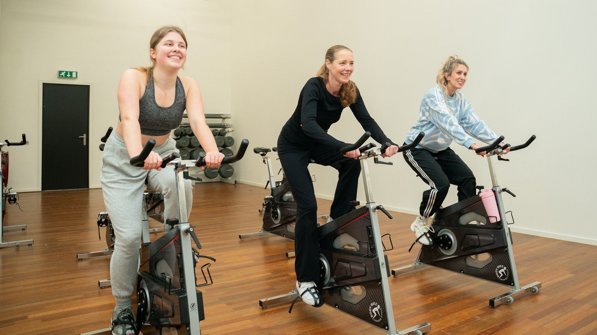 Drie vrouwen fietsen op hometrainers in een sportschool.