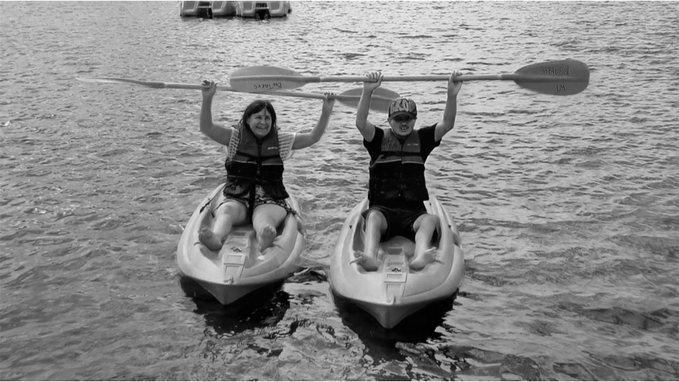 Black and white photos of two people sitting in seperate kayaks holding paddles abive their heads