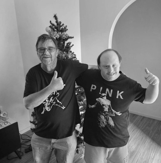 Black and white image of two males standing in front of a Christmas tree with thumbs up