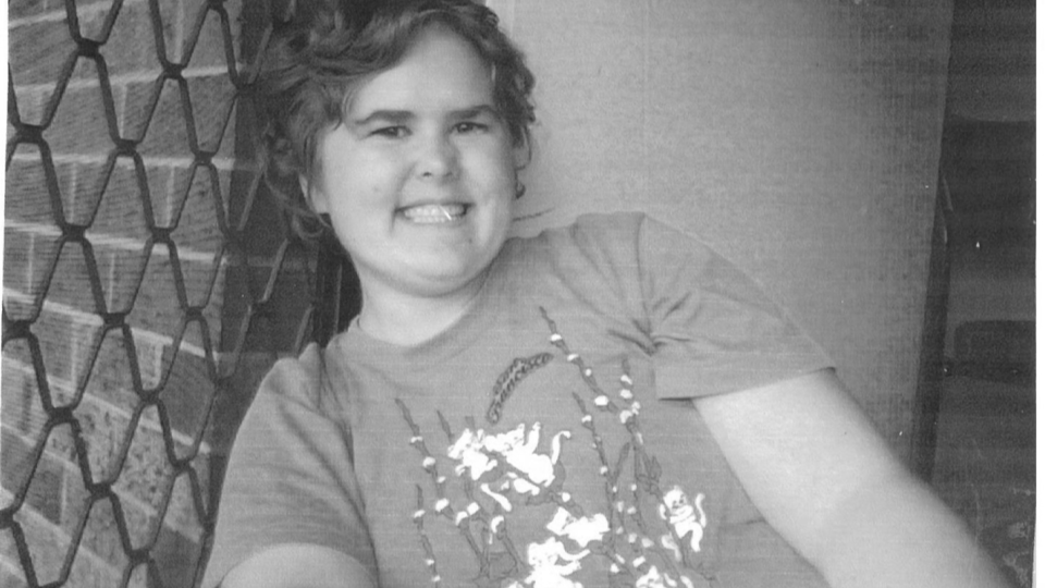 Black and white image of a young female sitting against a door smiling