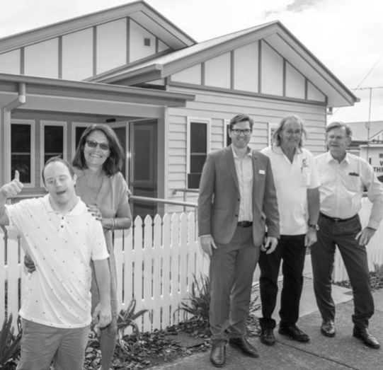 4 males and a female smiling outside of a house