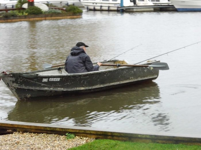 Fisherman in fishing dinghy by Wherry cottage mooring.