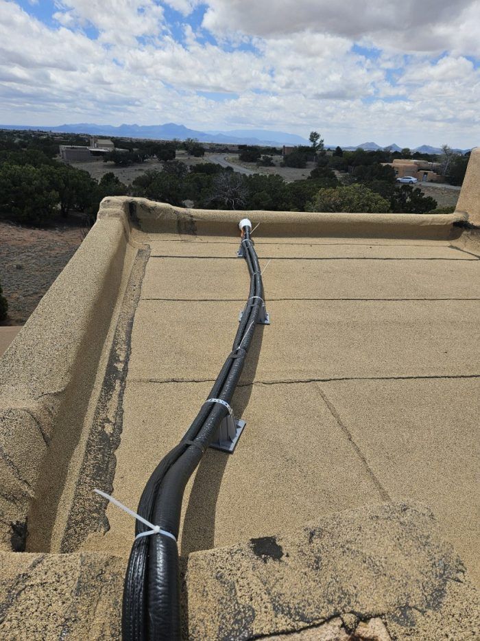 View from rooftop of black cables secured with white ties, background of trees and mountains.