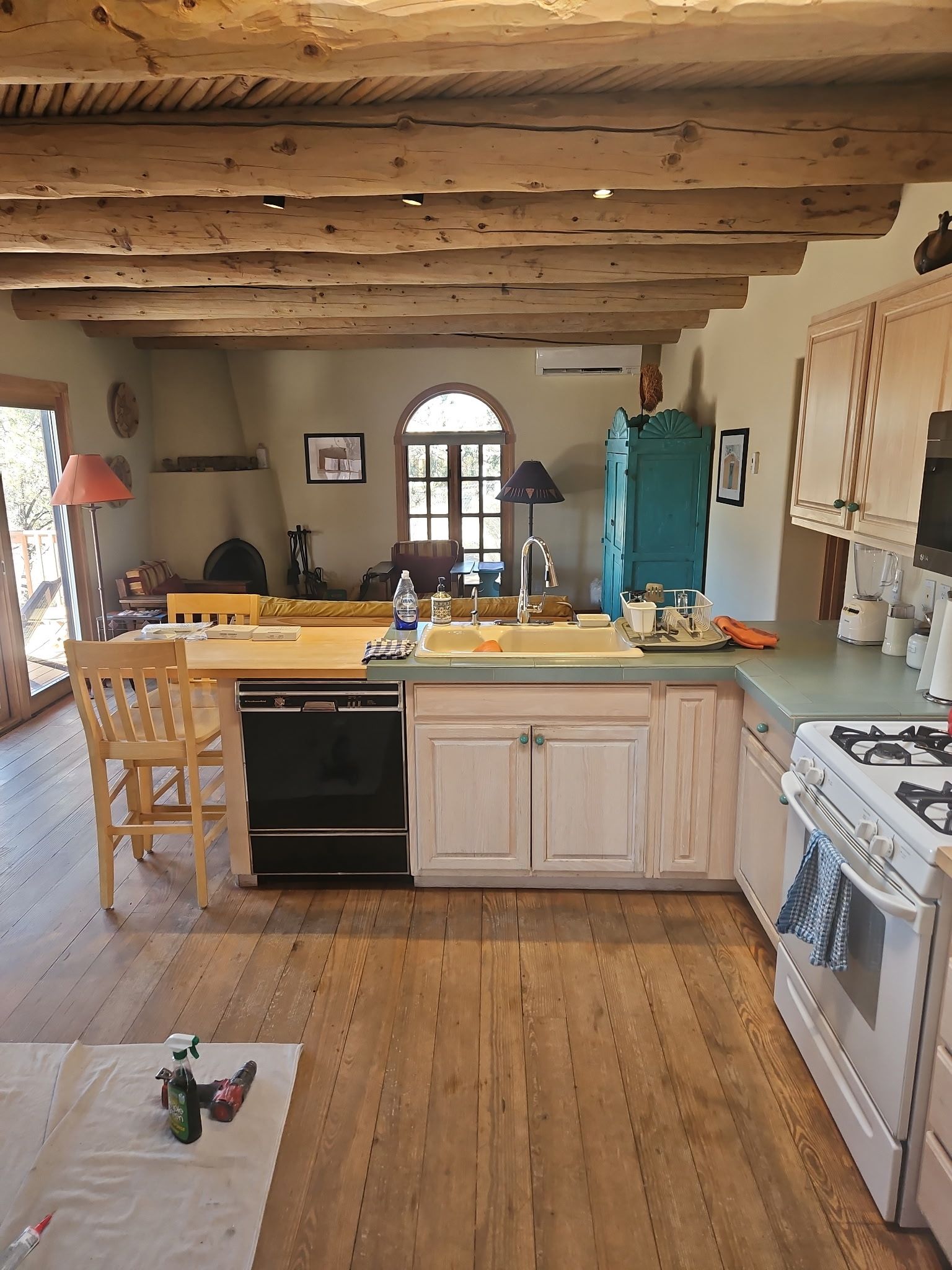 Kitchen with wood ceiling beams, light wood floor, white cabinets, black appliances, and turquoise cabinet.