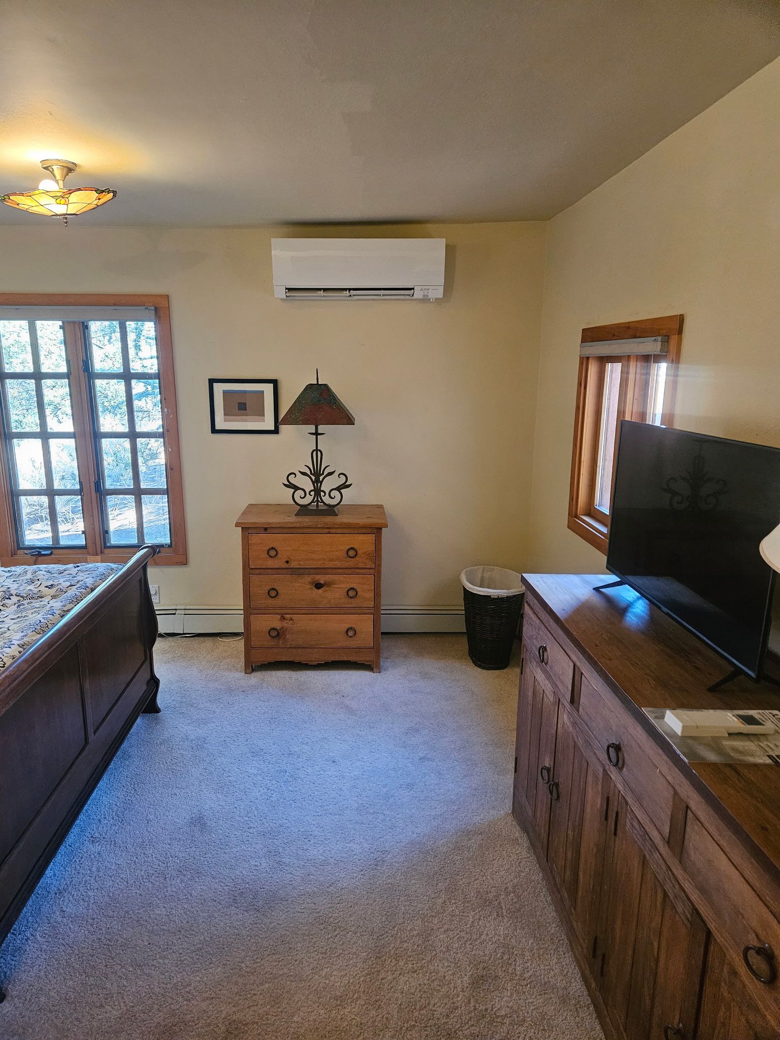 Bedroom with wooden furniture, beige walls, and a window. An AC unit is mounted on the wall.